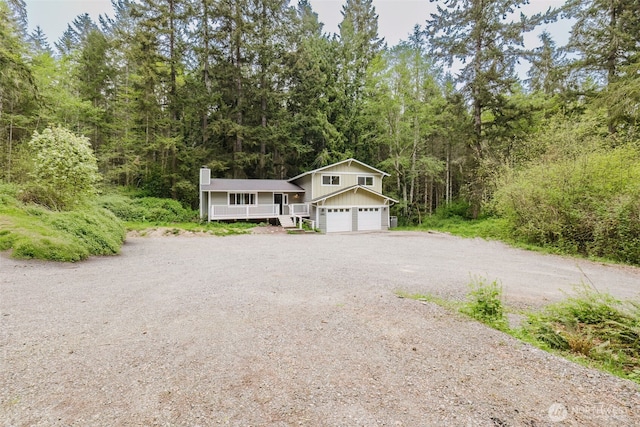 view of front of home featuring a chimney, dirt driveway, board and batten siding, an attached garage, and a view of trees