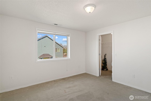 unfurnished bedroom featuring a walk in closet, carpet flooring, a textured ceiling, and visible vents