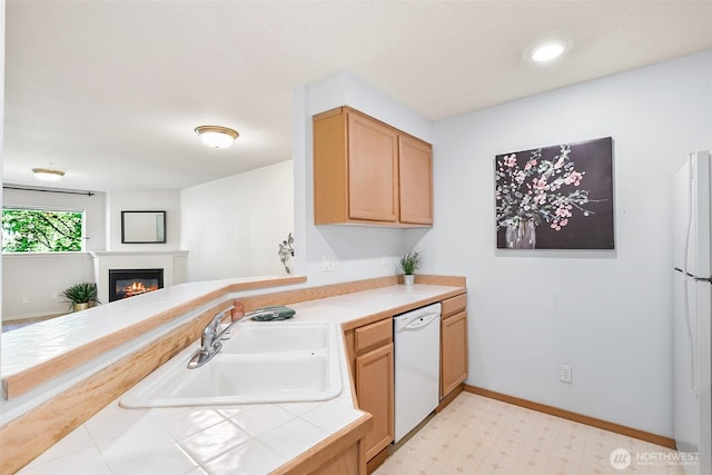 kitchen featuring a glass covered fireplace, white appliances, light floors, tile counters, and a sink