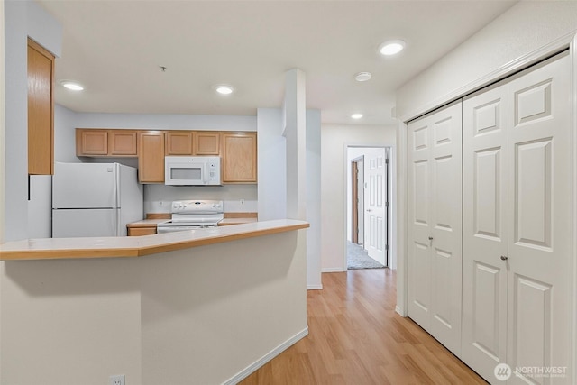 kitchen with light wood-type flooring, light countertops, baseboards, a peninsula, and white appliances