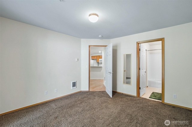 unfurnished bedroom with visible vents, freestanding refrigerator, baseboards, carpet flooring, and ensuite bath