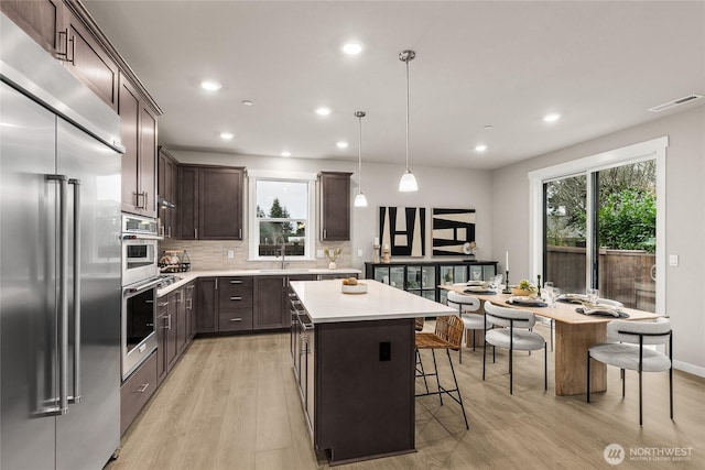 kitchen featuring dark brown cabinets, appliances with stainless steel finishes, a sink, light wood-style floors, and visible vents