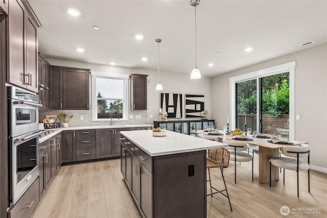 kitchen with a center island, stainless steel double oven, light wood-style flooring, and dark brown cabinets