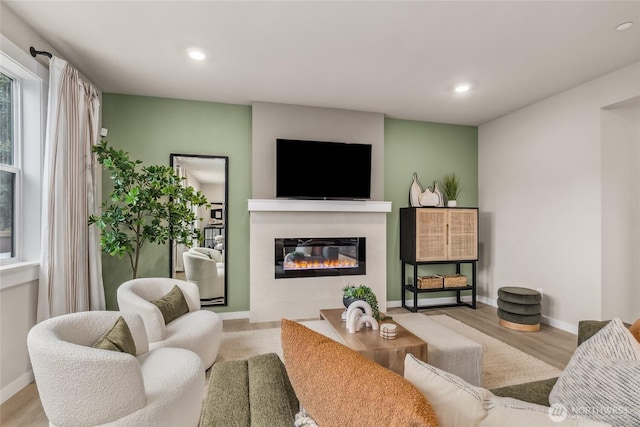 living area with recessed lighting, baseboards, a glass covered fireplace, and wood finished floors