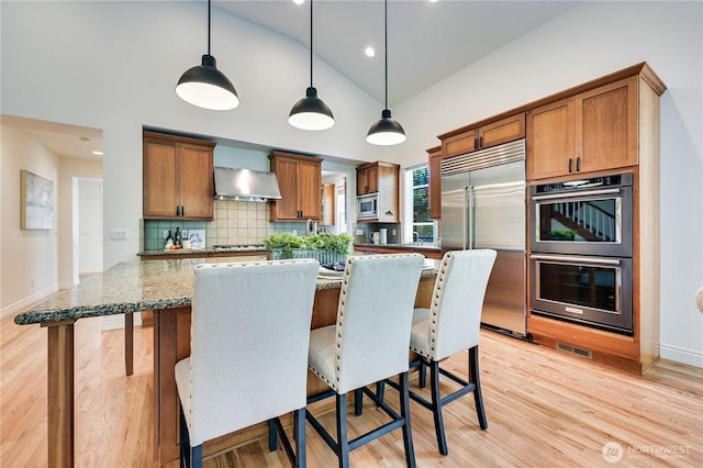 6722 Azalea Way SE, Snoqualmie, WA 98065 - kitchen with built in appliances, wall chimney range hood, hanging light fixtures, decorative backsplash, and stone countertops