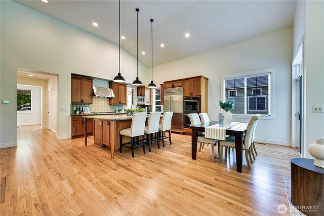 6722 Azalea Way SE, Snoqualmie, WA 98065 - kitchen featuring wall chimney range hood, stainless steel built in fridge, high vaulted ceiling, a kitchen island, and a breakfast bar area