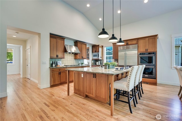 6722 Azalea Way SE, Snoqualmie, WA 98065 - kitchen with built in appliances, brown cabinetry, wall chimney exhaust hood, a kitchen bar, and light wood-type flooring