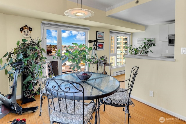 dining space with light wood-type flooring, a baseboard radiator, baseboards, and crown molding