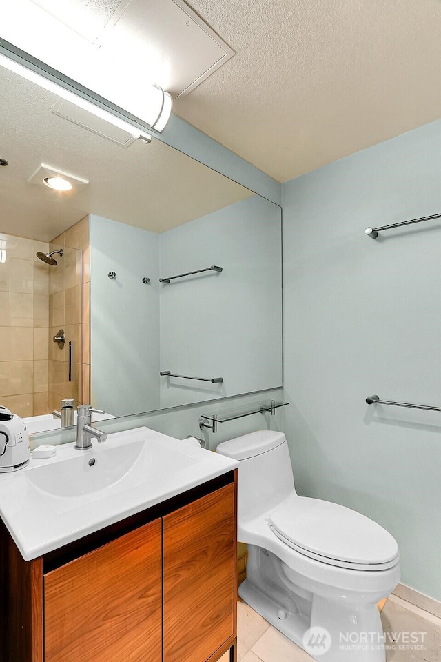 bathroom with a textured ceiling, walk in shower, vanity, tile patterned floors, and toilet
