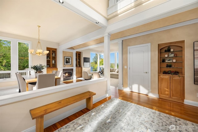 interior space with a lit fireplace, baseboards, a notable chandelier, and wood finished floors