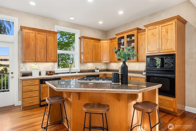 kitchen with a sink, glass insert cabinets, light wood-style floors, and black appliances