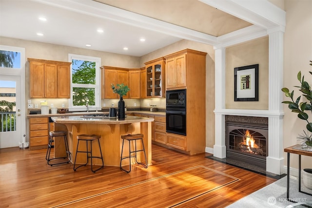 kitchen with wood finished floors, glass insert cabinets, a breakfast bar area, a fireplace with flush hearth, and black appliances