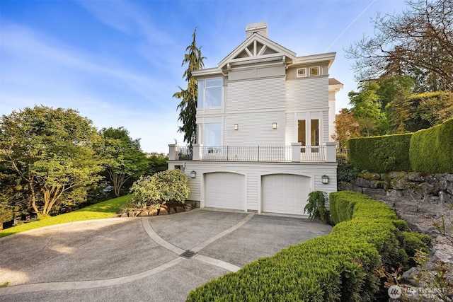exterior space featuring a chimney, french doors, a garage, a balcony, and aphalt driveway