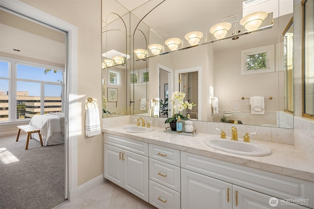 ensuite bathroom featuring a sink, baseboards, double vanity, and connected bathroom