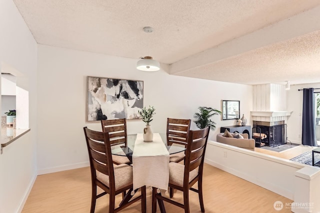 dining room with light wood-type flooring, baseboards, a textured ceiling, and a multi sided fireplace