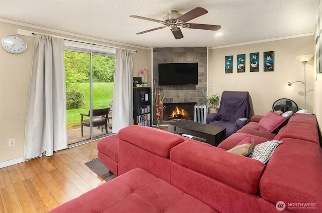 living area with a stone fireplace, ornamental molding, ceiling fan, and wood finished floors