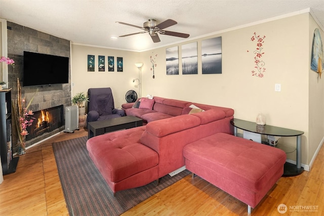 living room featuring ceiling fan, crown molding, a fireplace, radiator heating unit, and light wood-style flooring