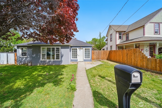 view of front of property featuring stucco siding, a fenced backyard, and a front lawn