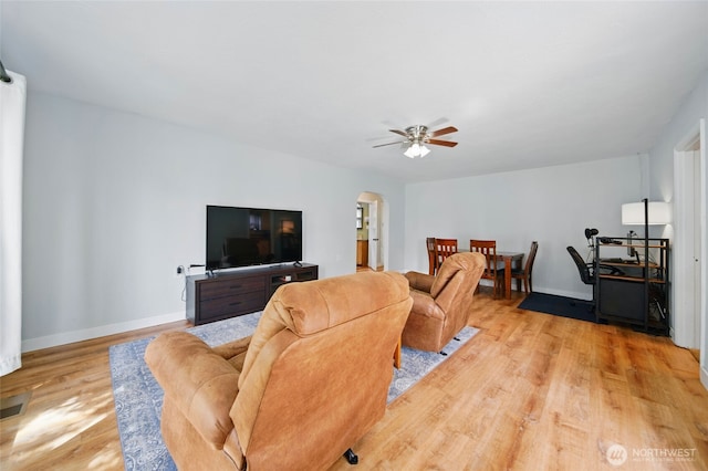 living area featuring light wood-type flooring, arched walkways, baseboards, and ceiling fan