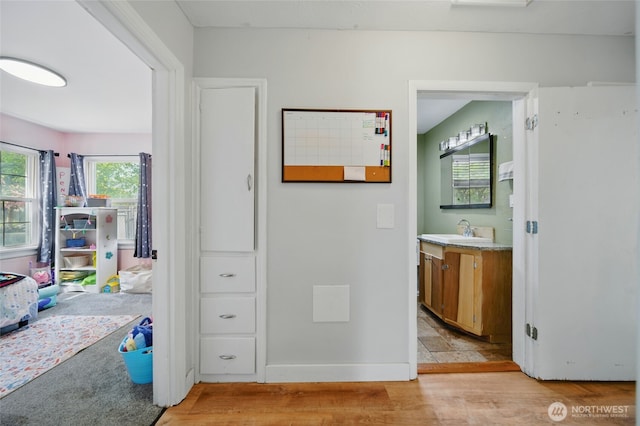 hall featuring baseboards, a sink, and light wood finished floors