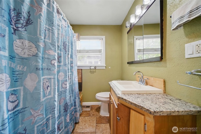 bathroom with stone tile floors, vanity, baseboards, toilet, and a shower with shower curtain