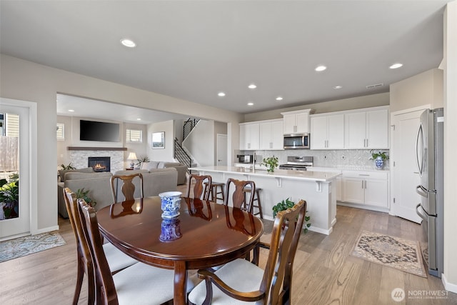 dining room with stairs, recessed lighting, light wood-style flooring, and a fireplace
