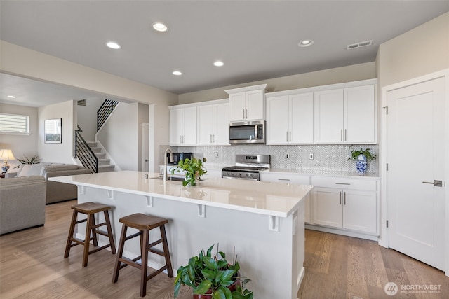 kitchen featuring appliances with stainless steel finishes, a breakfast bar, a sink, open floor plan, and visible vents