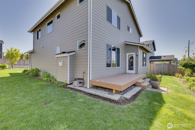 rear view of property with fence, a wooden deck, and a lawn