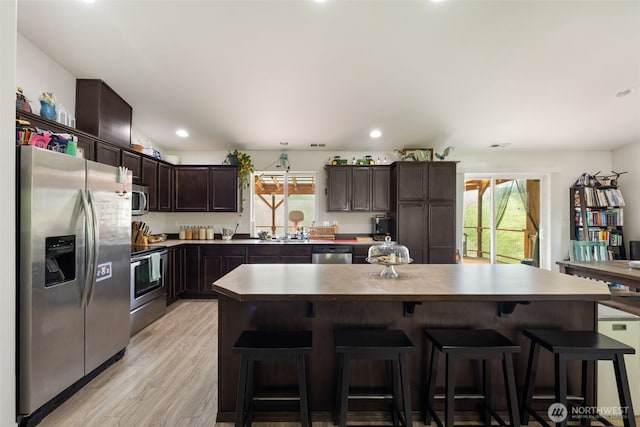 29304 39th Ave E, Graham, WA 98338 - kitchen featuring dark brown cabinets, appliances with stainless steel finishes, a breakfast bar, light wood-type flooring, and a kitchen island