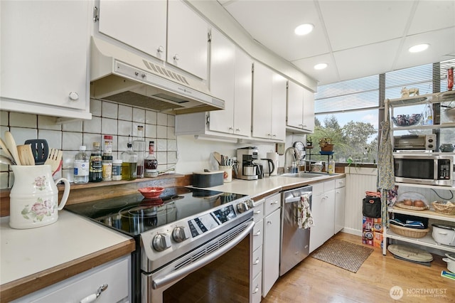 kitchen featuring white cabinets, a sink, light wood-style floors, stainless steel appliances, and under cabinet range hood