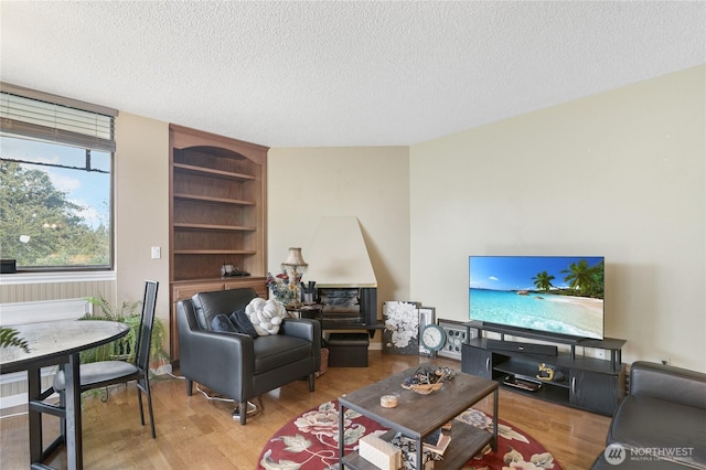 living area featuring built in shelves, a textured ceiling, and wood finished floors