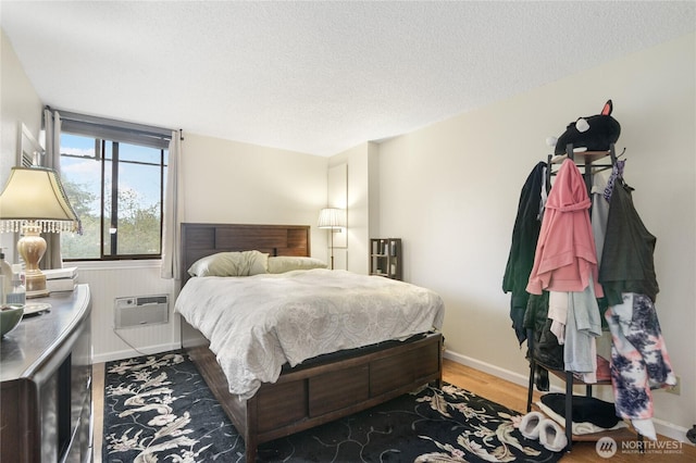 bedroom featuring baseboards, a textured ceiling, a wall unit AC, and wood finished floors