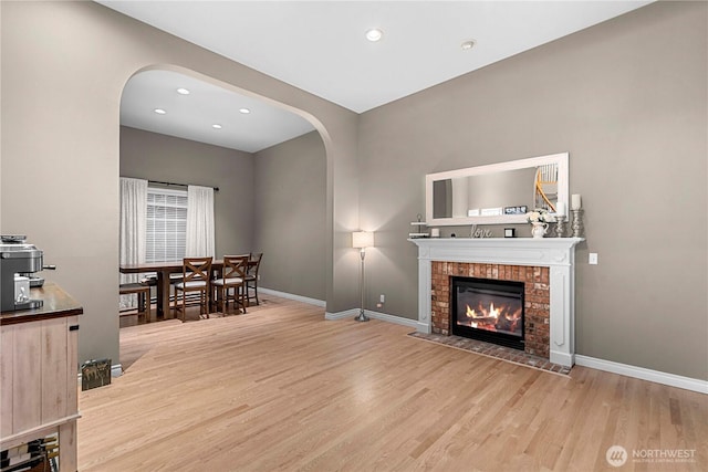 living area with baseboards, arched walkways, a brick fireplace, and wood finished floors