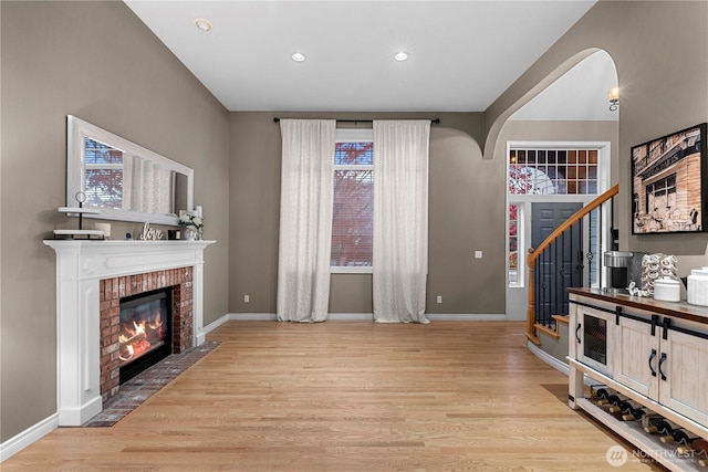 unfurnished living room with a fireplace, light wood-style floors, baseboards, stairway, and recessed lighting
