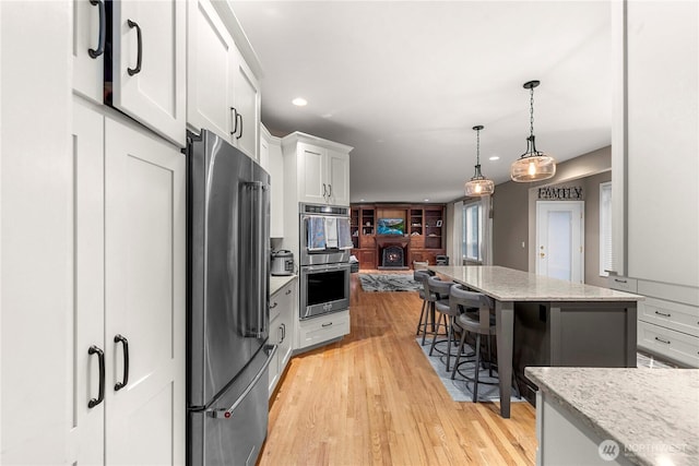 kitchen featuring appliances with stainless steel finishes, light stone countertops, white cabinets, light wood-style floors, and recessed lighting
