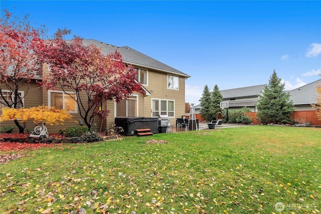 rear view of property with fence, a lawn, and a hot tub