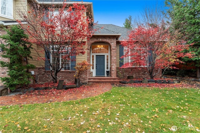 view of front of property featuring brick siding, a shingled roof, and a front yard