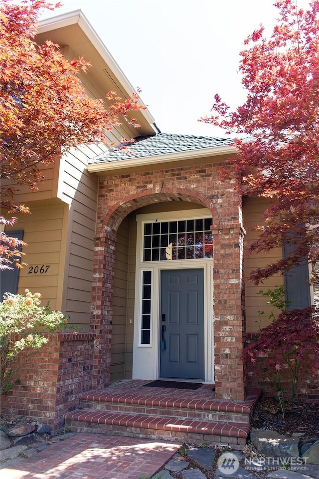 entrance to property with brick siding and a shingled roof