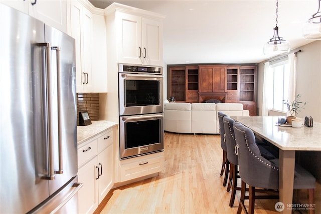 kitchen featuring light wood-type flooring, white cabinets, light stone counters, appliances with stainless steel finishes, and backsplash