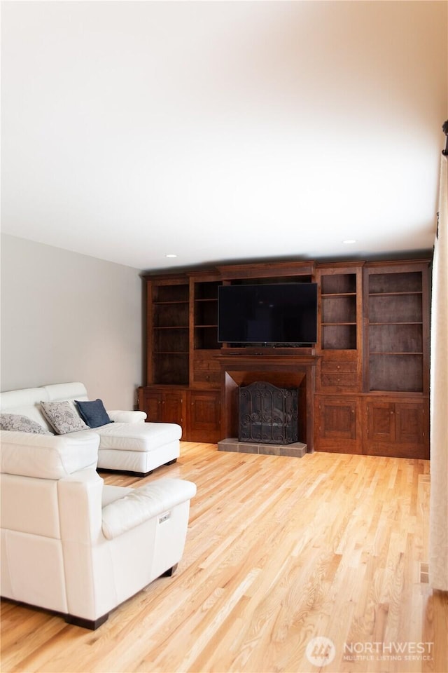 living area featuring a fireplace with raised hearth, recessed lighting, and wood finished floors