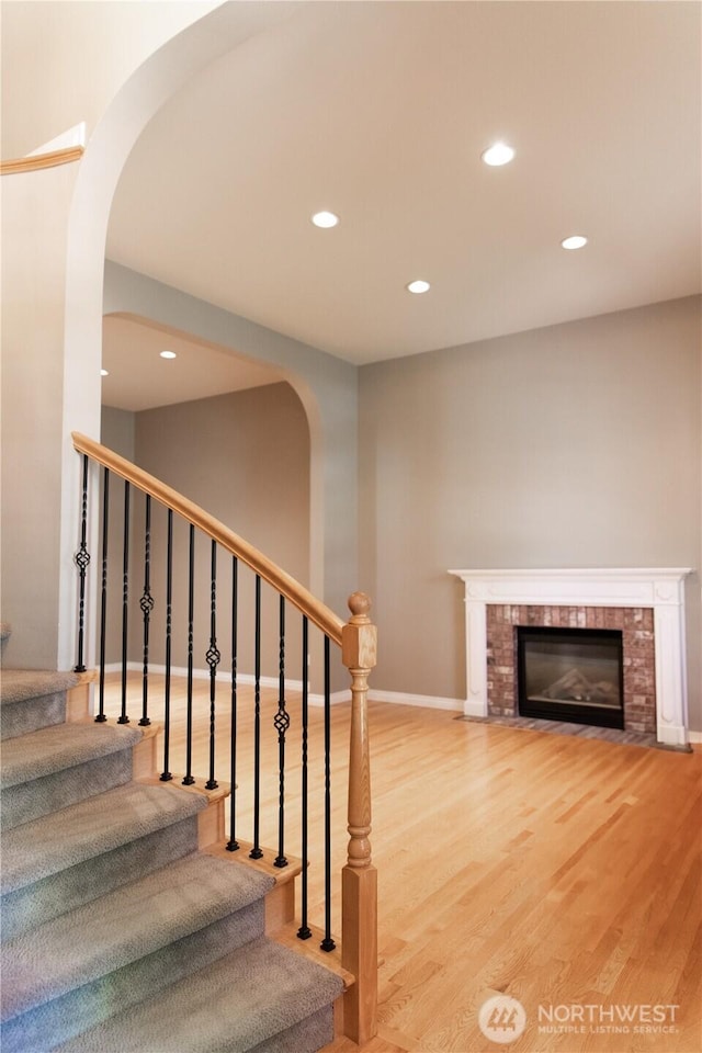 stairway featuring wood finished floors, a fireplace, baseboards, recessed lighting, and arched walkways