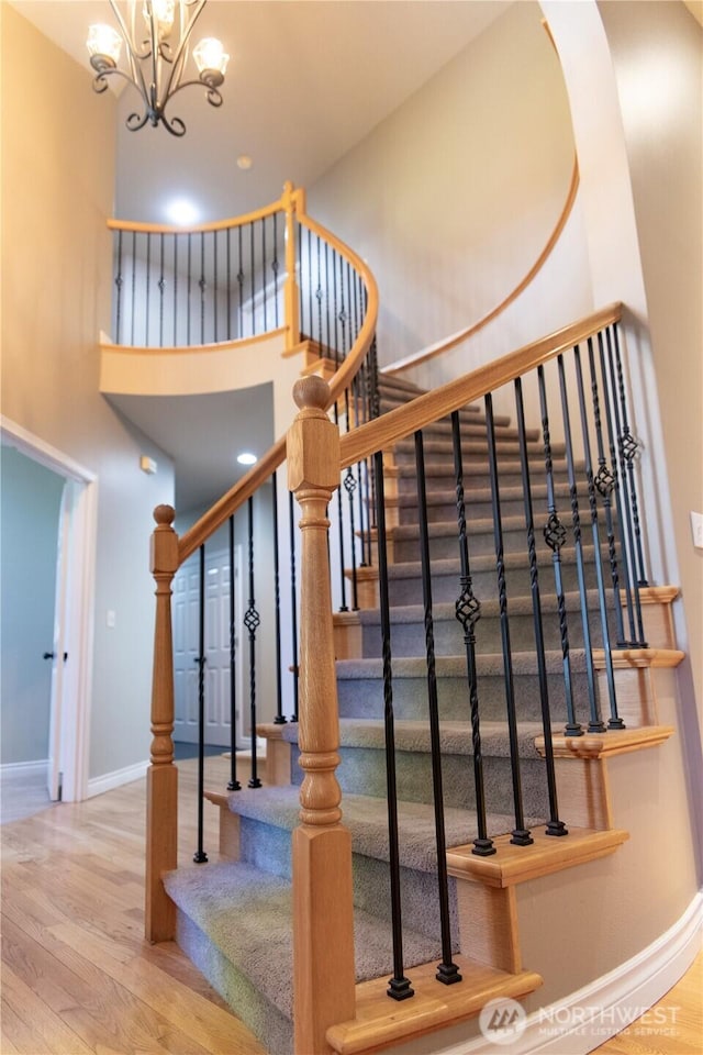 staircase featuring baseboards, arched walkways, wood finished floors, and an inviting chandelier
