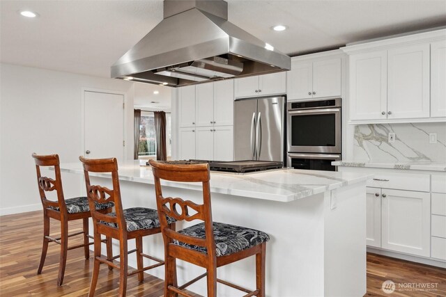 18 SE 18th St, Battle Ground, WA 98604 - kitchen with island range hood, appliances with stainless steel finishes, light wood finished floors, white cabinets, and a kitchen bar