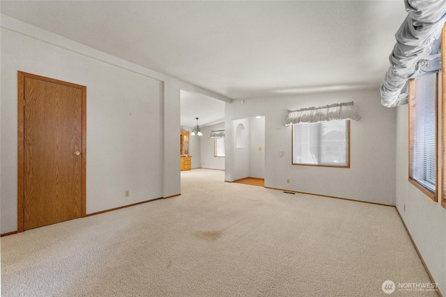 carpeted empty room with baseboards, a notable chandelier, and lofted ceiling
