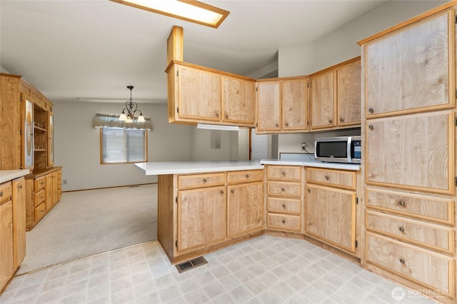 kitchen with light brown cabinets, light countertops, a peninsula, stainless steel microwave, and light floors