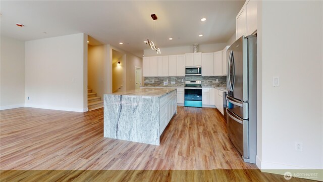 15941 Glenwood Rd SW, Port Orchard, WA 98367 - kitchen with light stone countertops, a center island, white cabinetry, light wood-style flooring, and appliances with stainless steel finishes