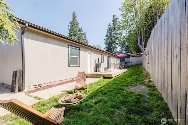view of side of property with a wooden deck, a patio, a fenced backyard, crawl space, and a lawn