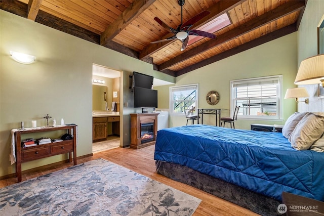 bedroom with connected bathroom, lofted ceiling with beams, light wood finished floors, a glass covered fireplace, and wood ceiling