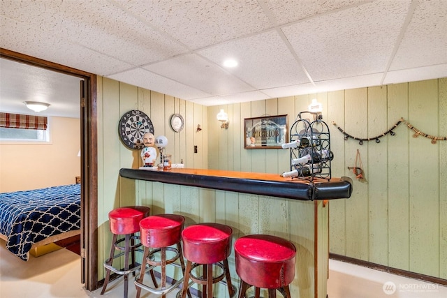 bar featuring a dry bar, a drop ceiling, and wooden walls