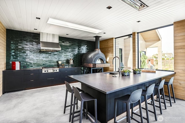 1721 J B George Rd, Walla Walla, WA 99362 - kitchen with a sink, wall chimney range hood, a breakfast bar, concrete floors, and wood walls